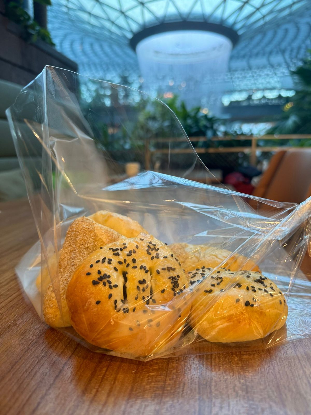 A bag of sesame-topped buns on a table, with an indoor waterfall behind