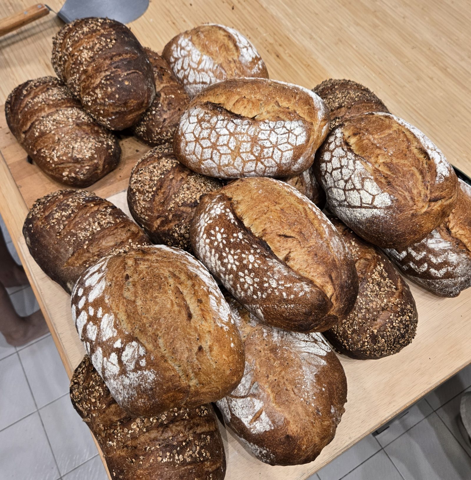 A table piled with sourdough loaves, some stencilled with flour patterns, some topped with oats