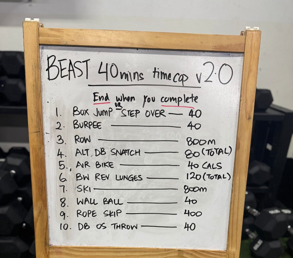 A whiteboard with the day's 40-minute workout: box jumps, burpees, row, snatches, air bike, lunges, ski, wall balls, rope skips and throws