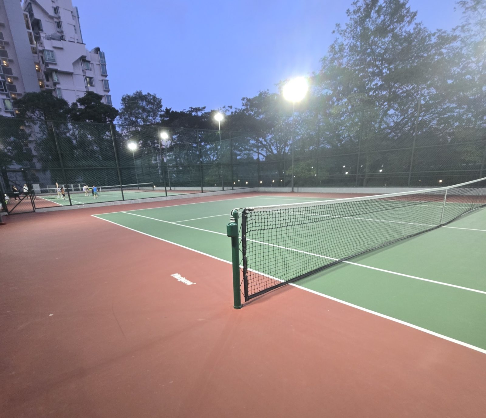 A floodlit outdoor tennis court at dusk